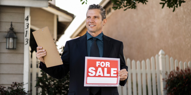 A "For Sale By Owner" sign posted in front of a residential house