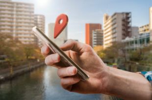Una persona sonriendo mientras usa su teléfono para buscar "hoteles cerca de mí" en un mapa, mostrando la facilidad y conveniencia de la búsqueda de alojamiento por ubicación.