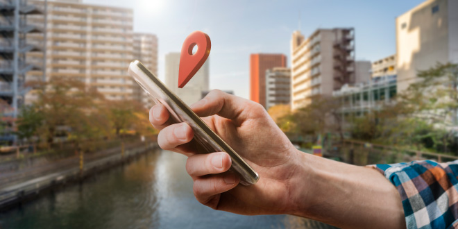 Una persona sonriendo mientras usa su teléfono para buscar "hoteles cerca de mí" en un mapa, mostrando la facilidad y conveniencia de la búsqueda de alojamiento por ubicación.