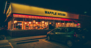 The iconic yellow sign of a Waffle House near me, glowing at dusk, inviting customers in.