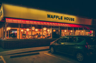 The iconic yellow sign of a Waffle House near me, glowing at dusk, inviting customers in.