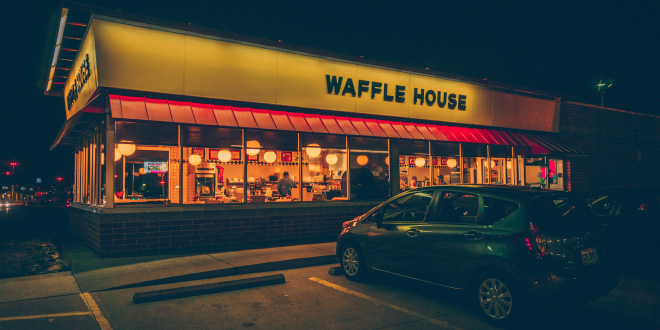 The iconic yellow sign of a Waffle House near me, glowing at dusk, inviting customers in.